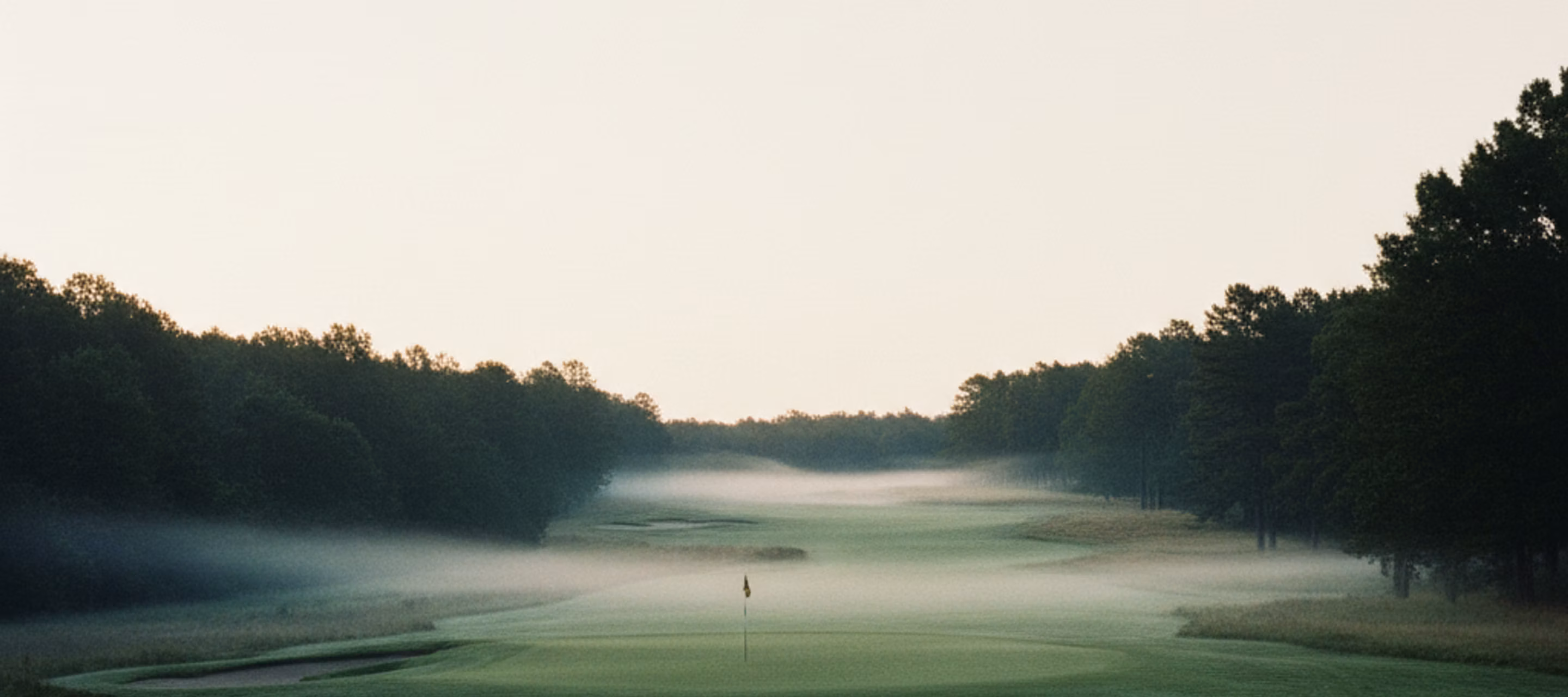 An empty fairway at first light, mist hanging low across the cut grass